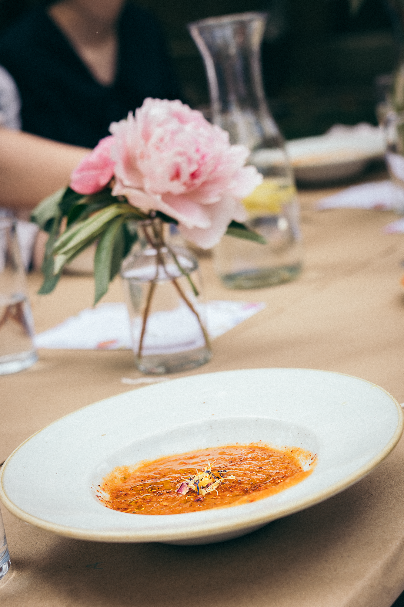 Orange creamy soup served in white bowl with pink peony flower centerpiece.