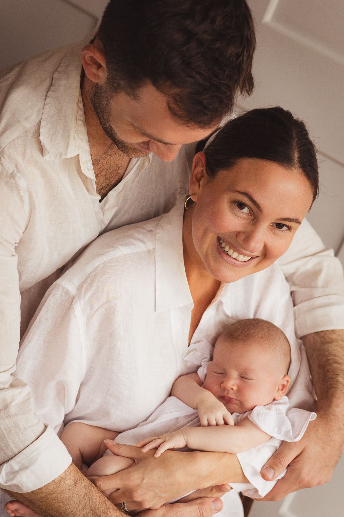 Intimate portrait of parent cradling newborn baby in white clothing.