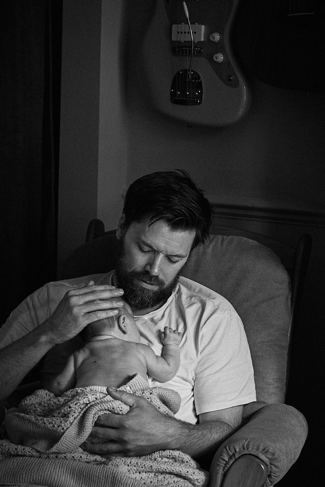 A black and white image showing a tender moment of bottle feeding in dim light.