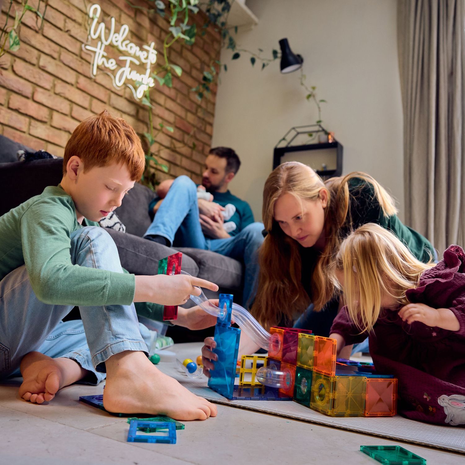 Family playing with colorful magnetic tiles on floor, children building together while parents relax in cozy living room.