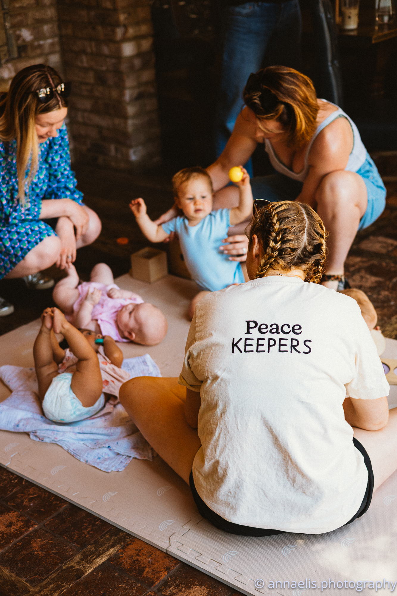 Baby and caregiver on floor mat with text visible on white clothing.