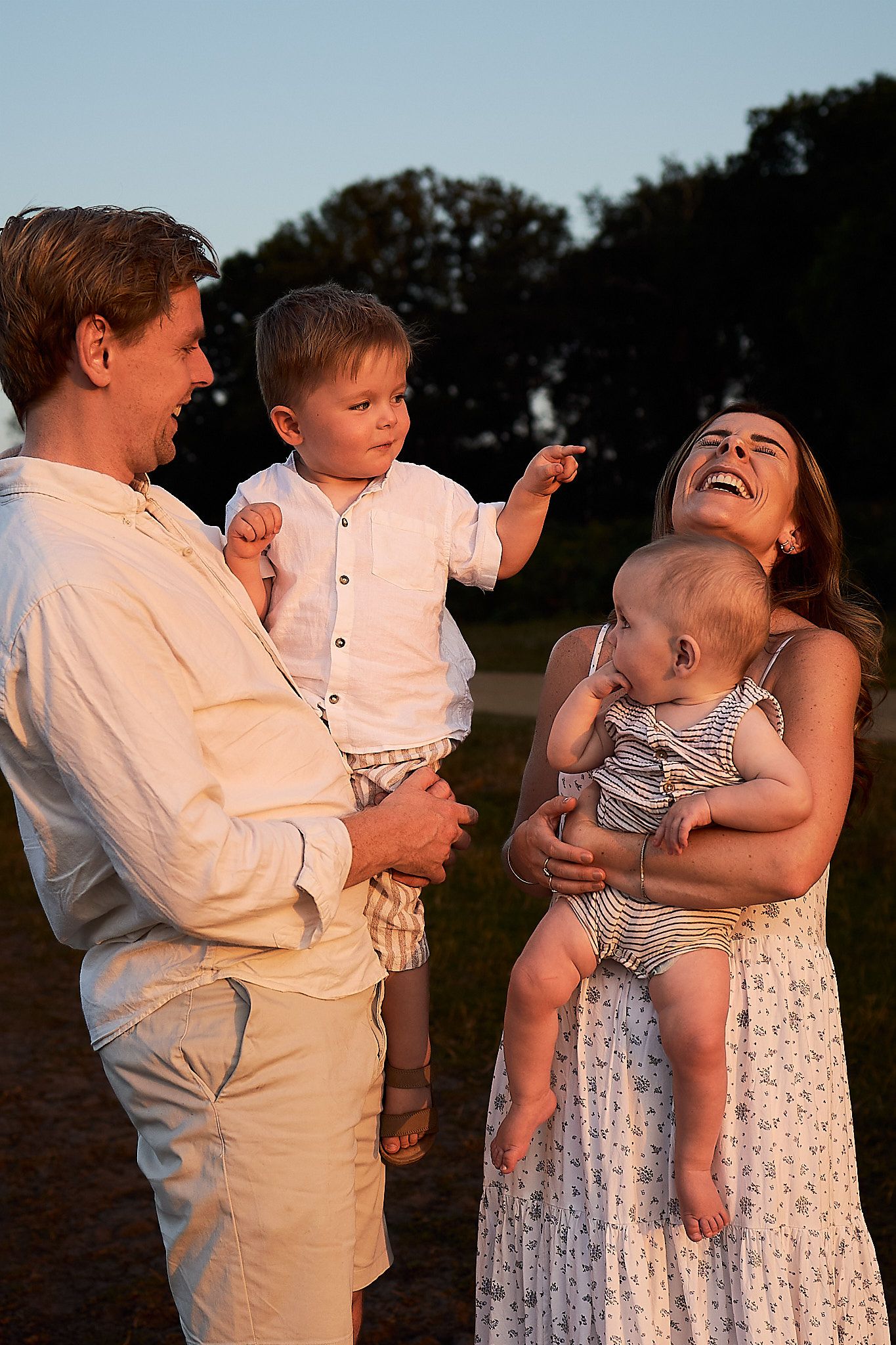 A family shares a joyful moment together outdoors during sunset, wearing light summer clothing.