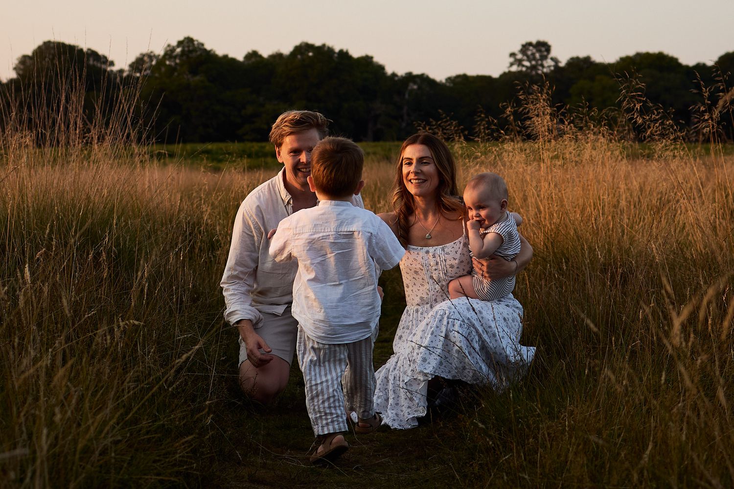 Candid family moments captured in warm evening light among tall grass.