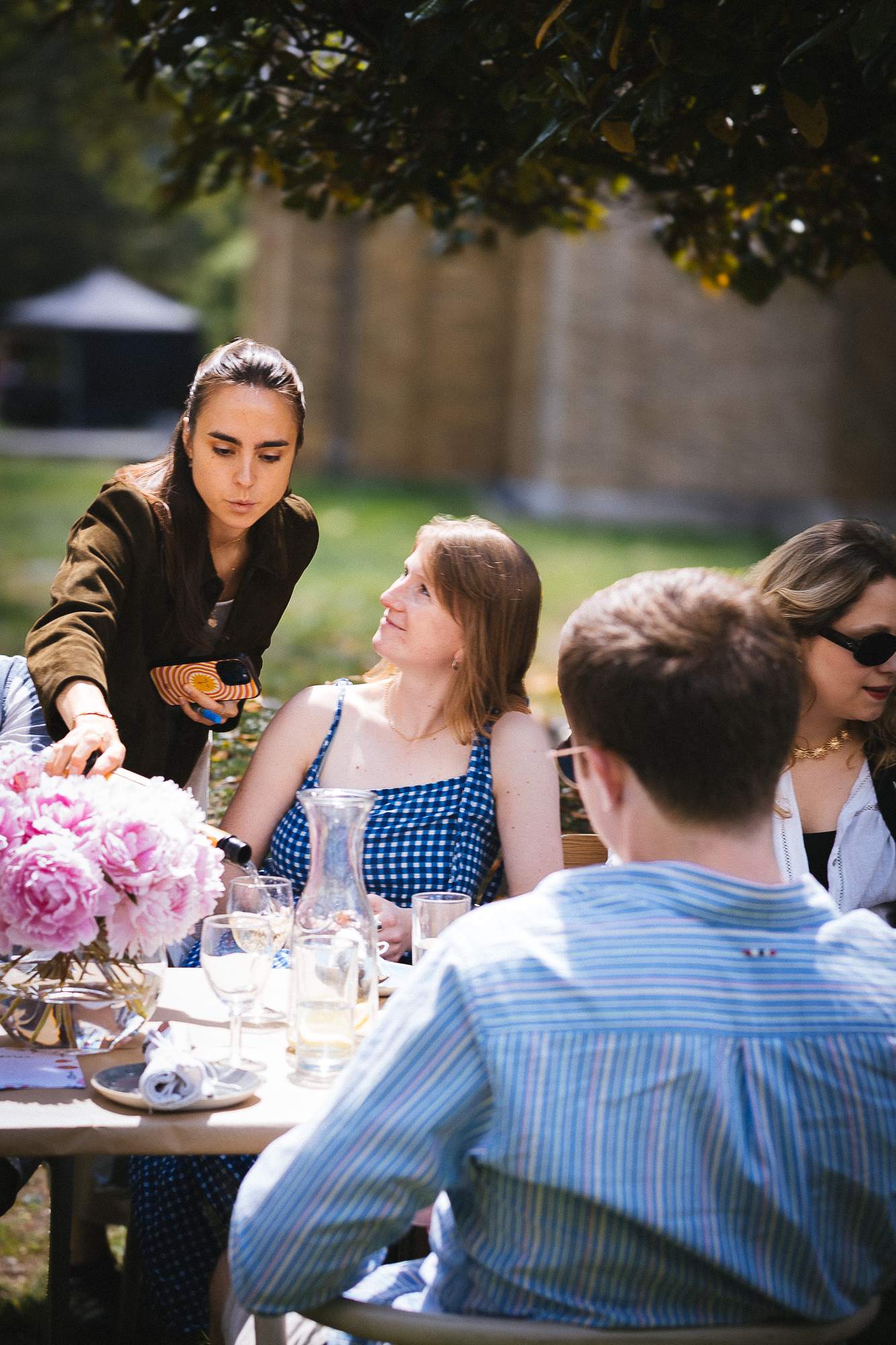 People gather around a table set with pink flowers for an outdoor meal.