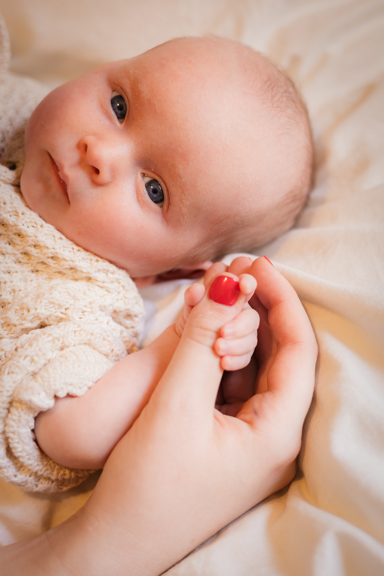 Sweet portrait of an infant in white lace clothing with hands gently touching their face.