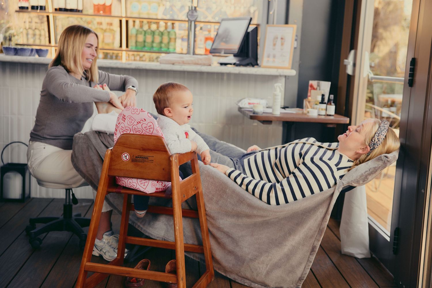 Two women enjoy a relaxed indoor setting with a baby in a wooden high chair.