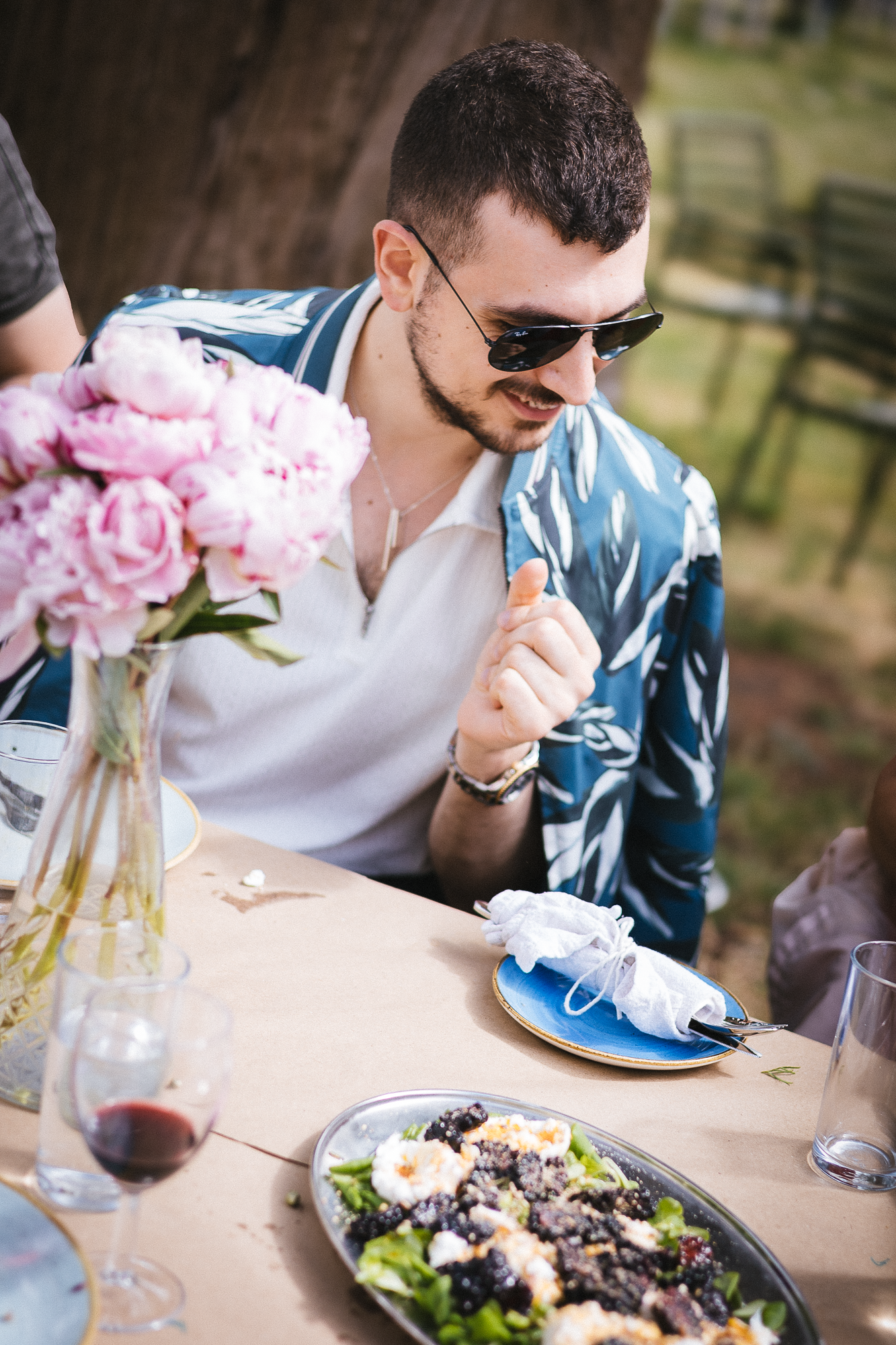 Elegant outdoor lunch setting with pink peonies and wine glasses on a white tablecloth.
