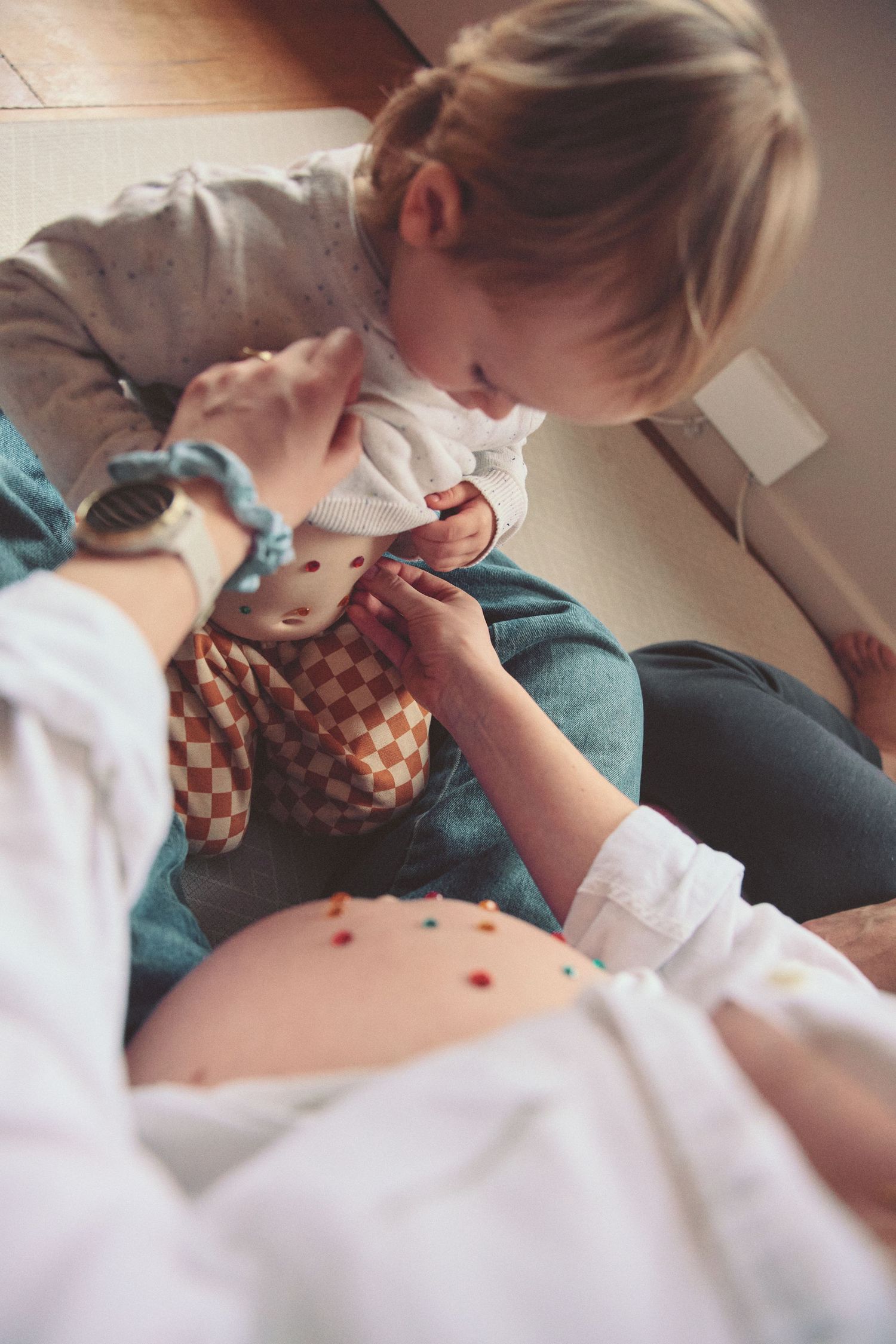 Toddler sitting on pregnant mother's lap playing with a stuffed toy while mom's bare belly is visible.