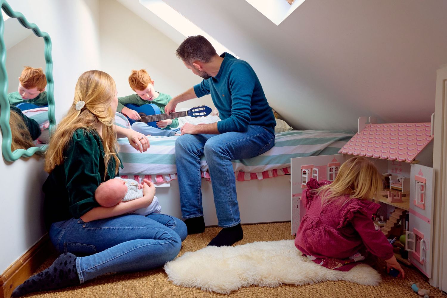 Family spending quality time together in a cozy attic bedroom, with father playing guitar while children play nearby.