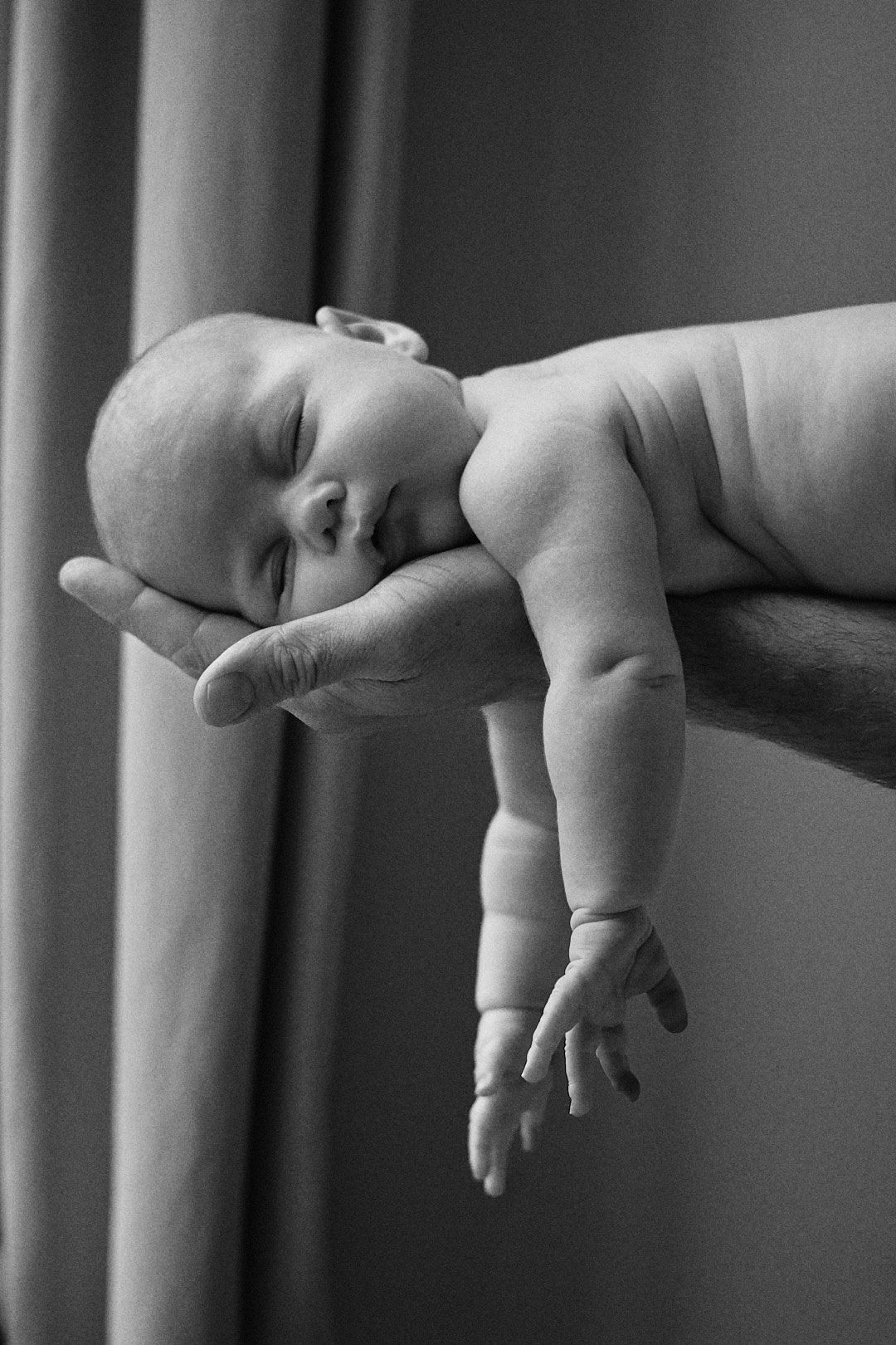 A sleeping infant rests peacefully on an adult's supportive hands in a black and white photograph.
