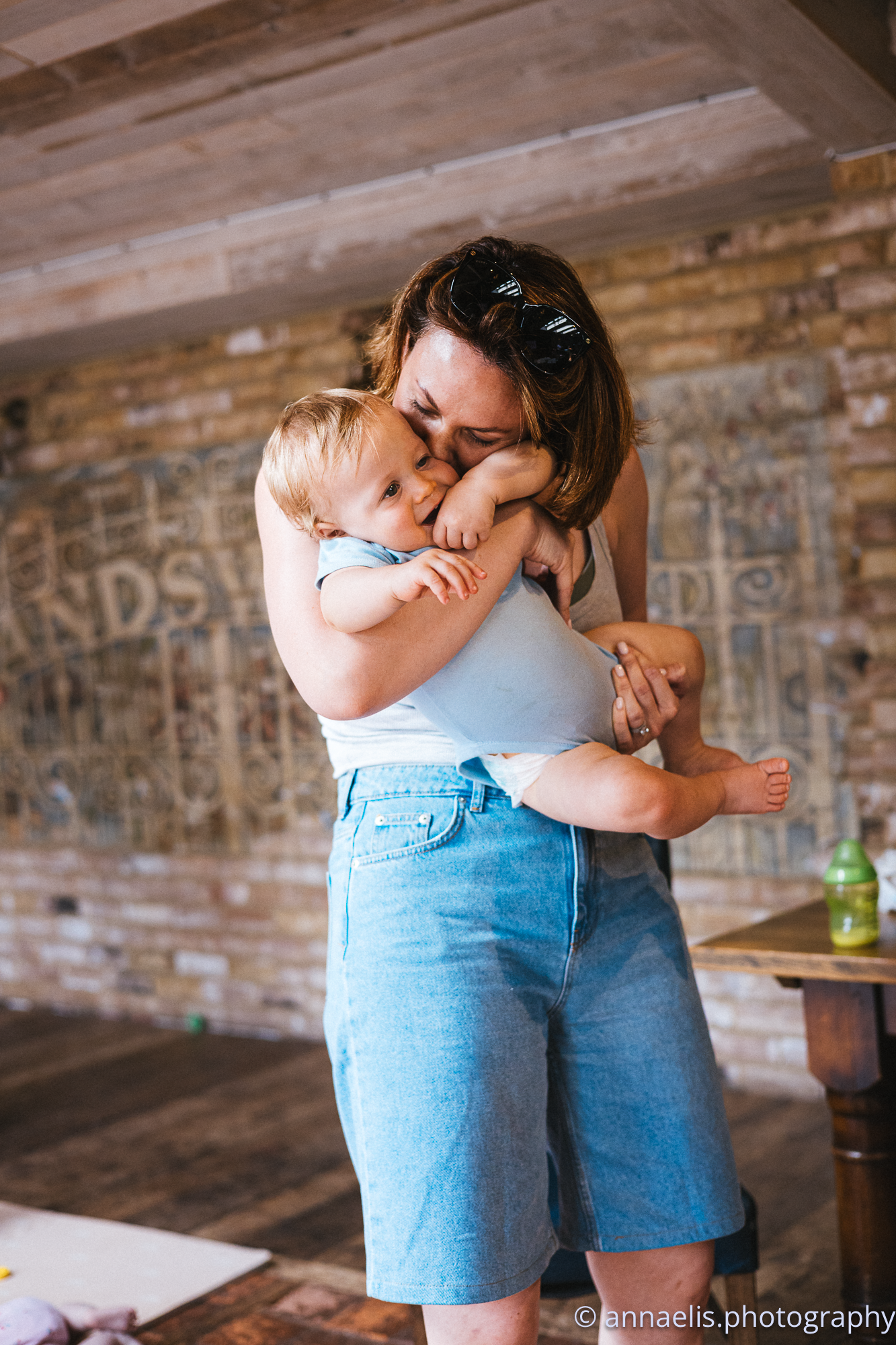 Parent and child share tender moment against exposed brick wall background.