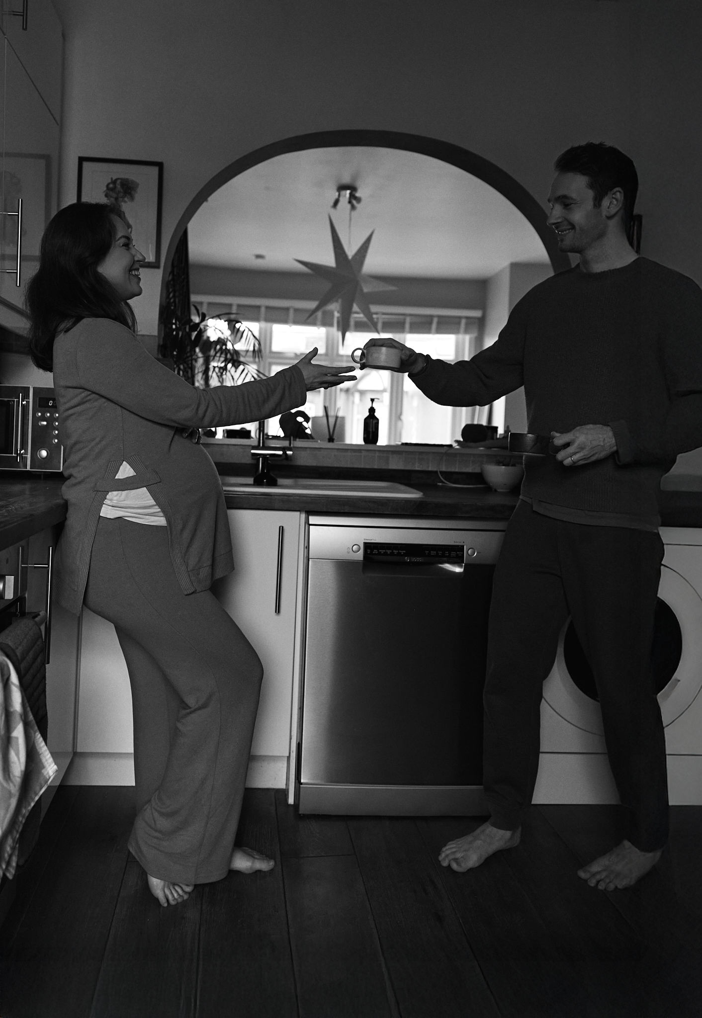 A couple dances joyfully in their kitchen, holding hands and smiling in a cozy home setting.