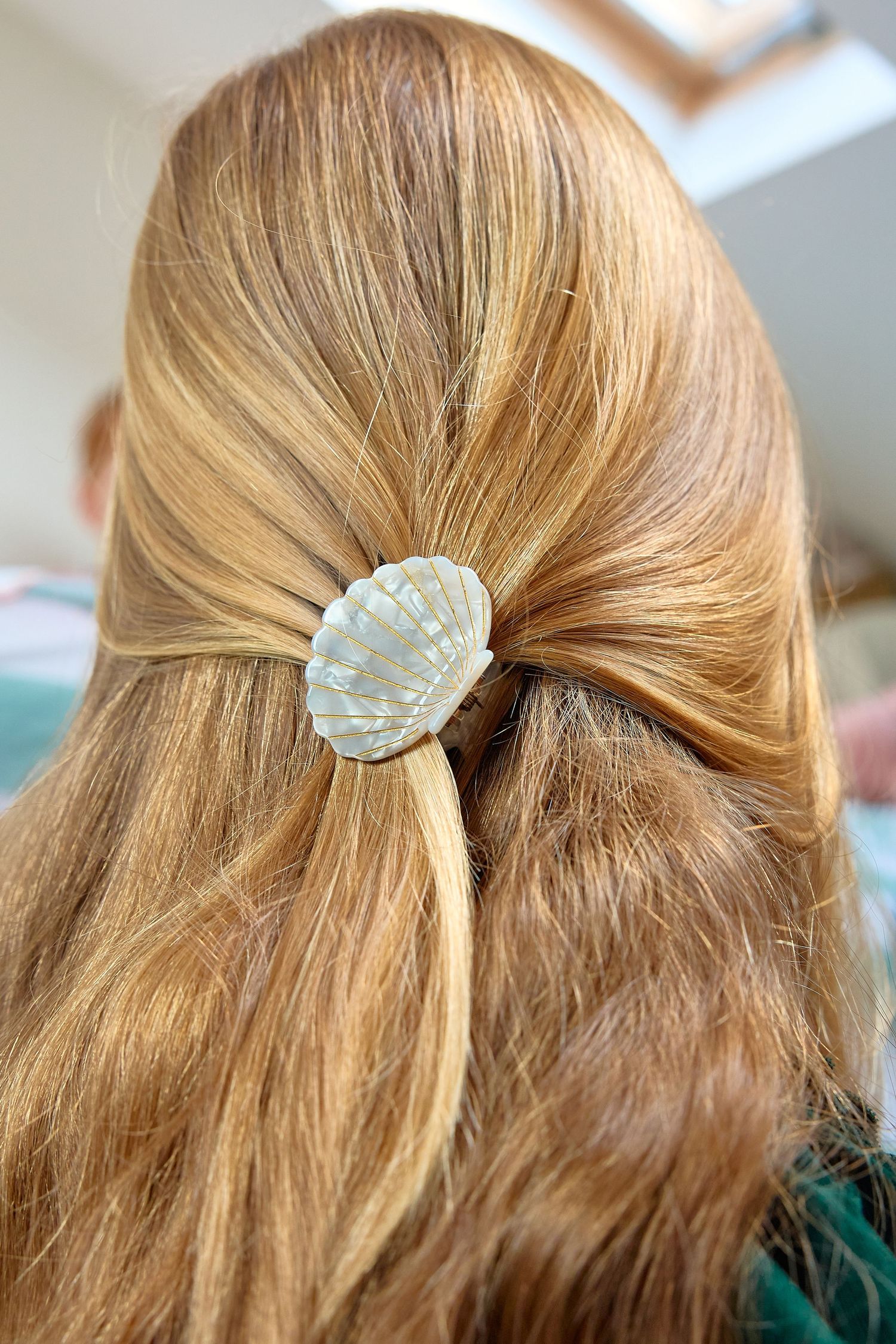 Close-up of red hair styled in a half-up ponytail secured with a decorative white seashell hair clip.