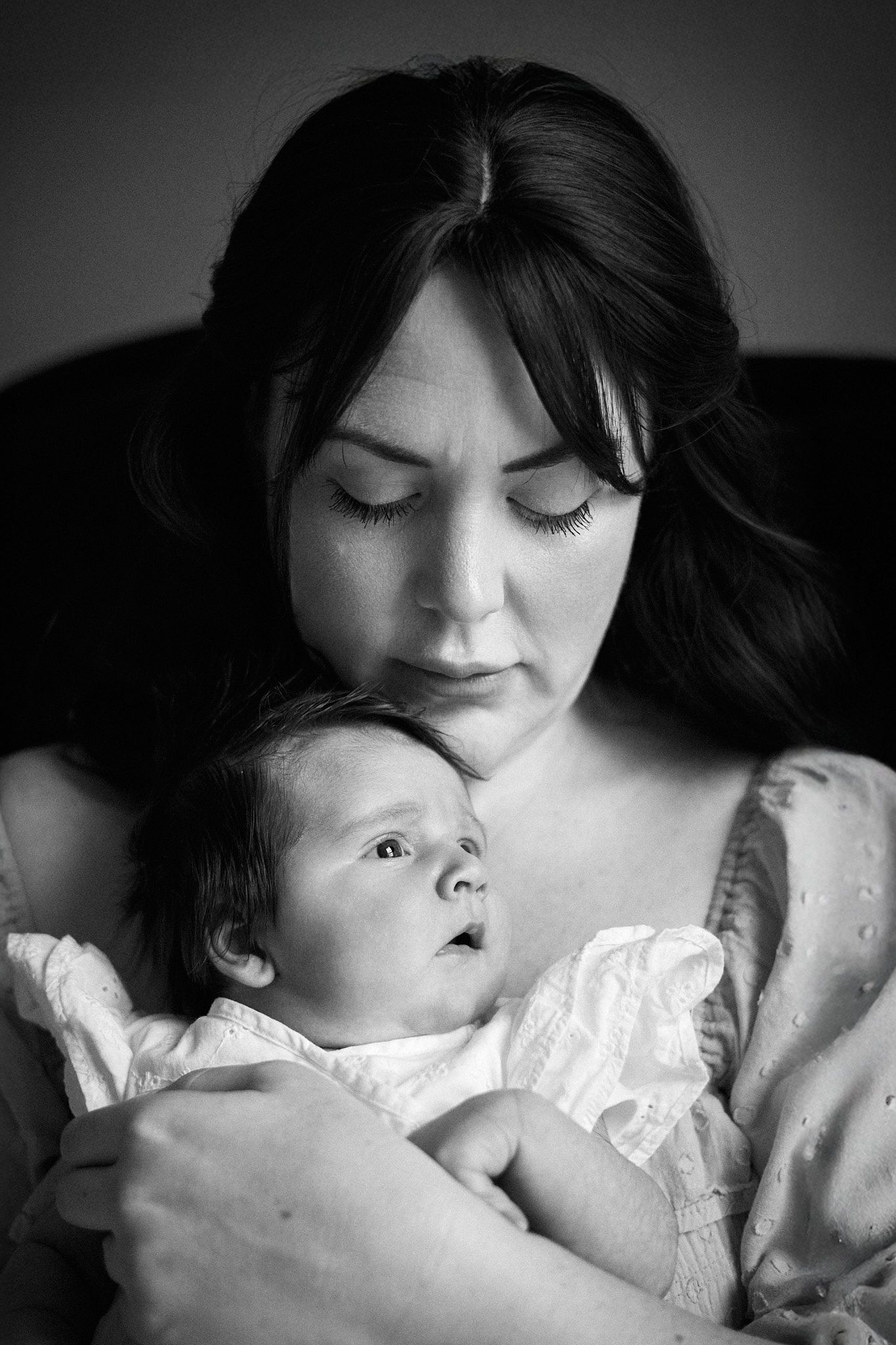 A dramatic black and white portrait showing a tender moment with an infant.