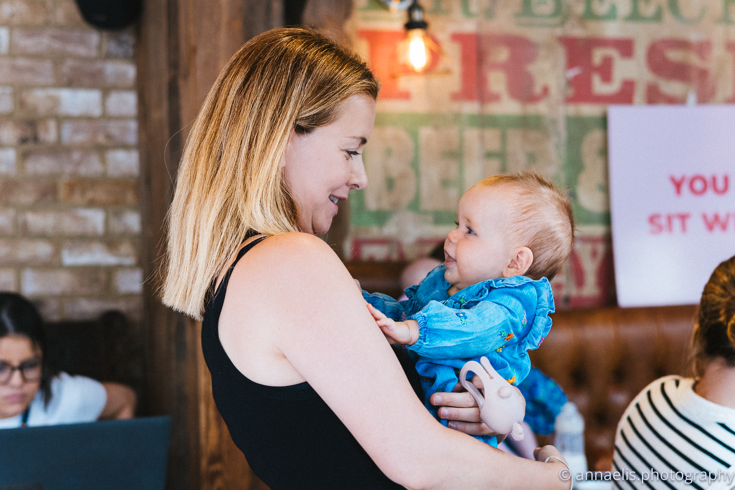 Parents with babies socialize in a restaurant with exposed brick walls.