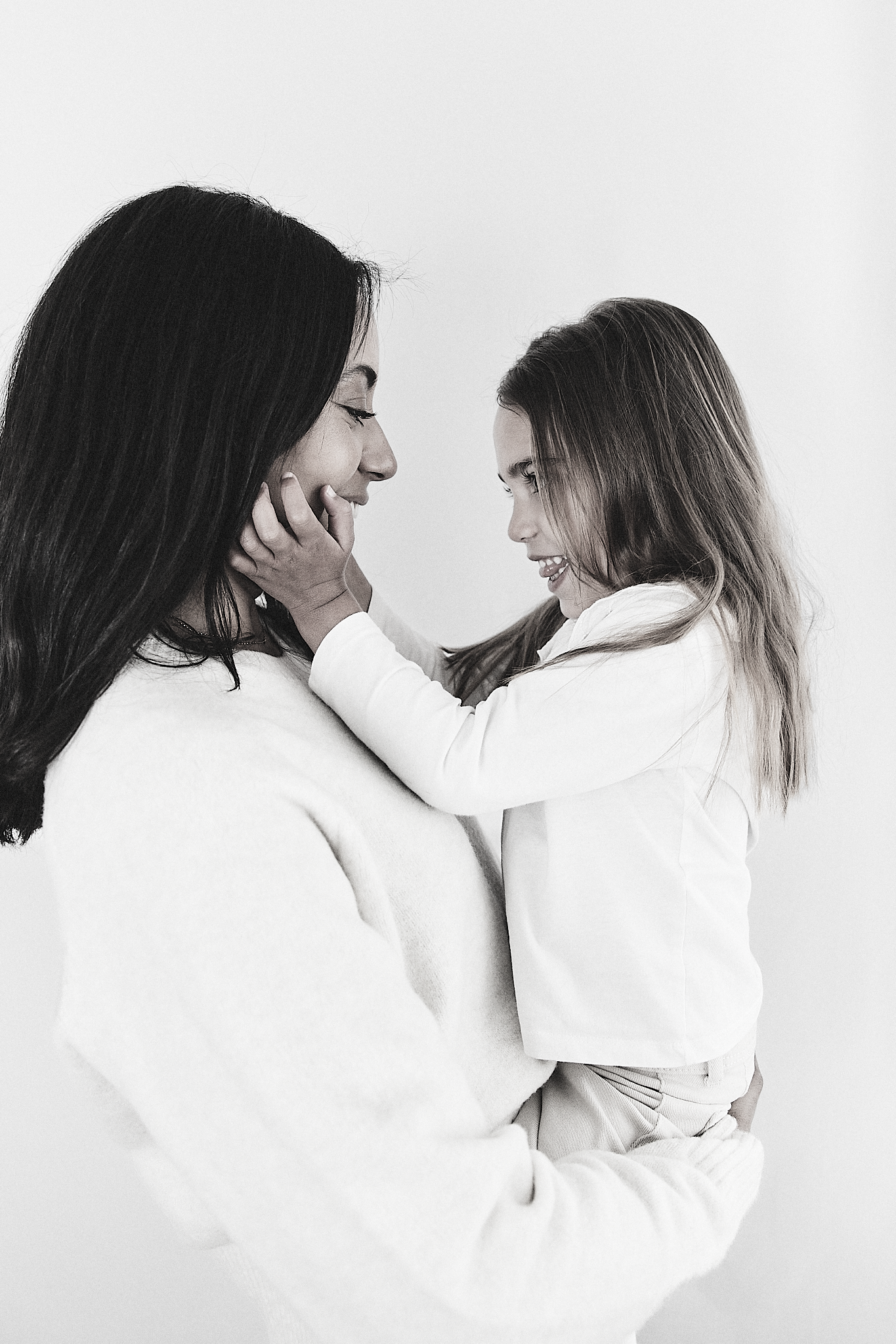 Black and white photo of a smiling mother holding her happy young daughter face to face.