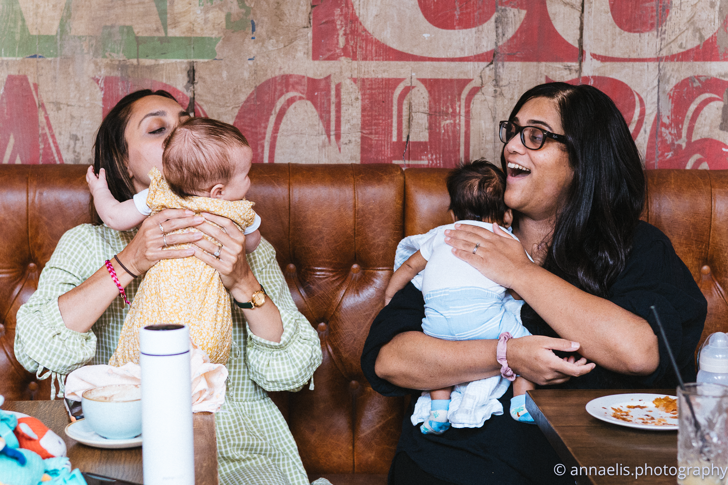Parents and infants socialize in a cozy restaurant setting with brick walls.