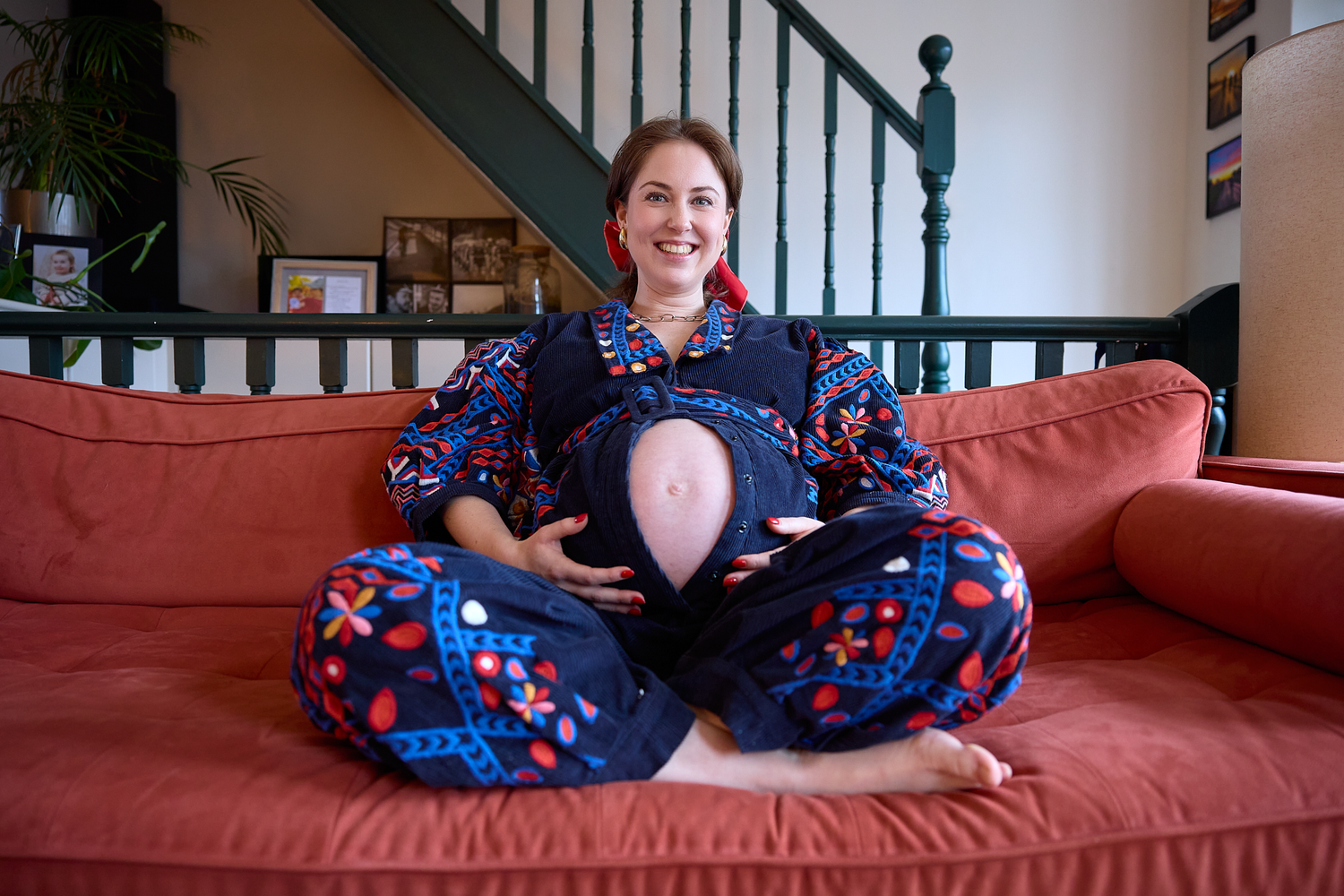 A person sits cross-legged on a red couch wearing a blue floral dress.