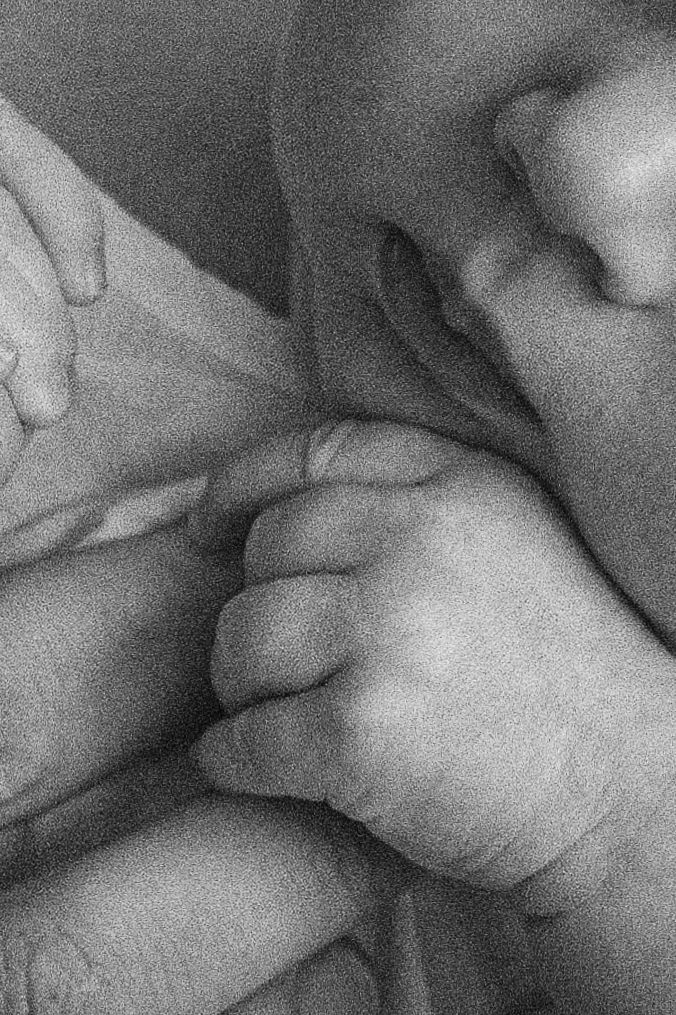 Black and white close-up photo of a newborn baby's tiny hand gently gripping an adult's finger.
