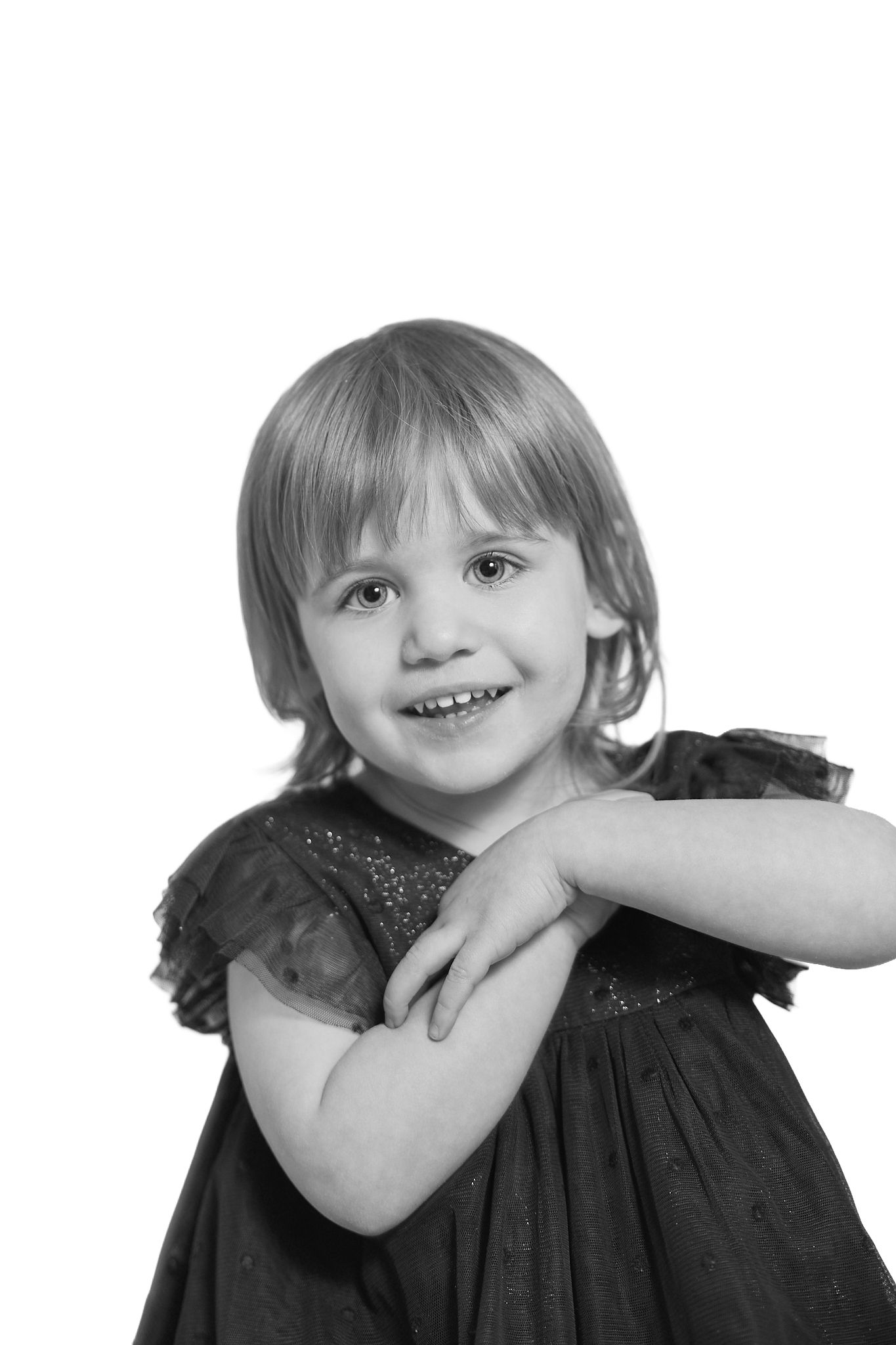 Black and white portrait of a smiling young blonde girl in a dark dress with arms crossed, isolated on white.