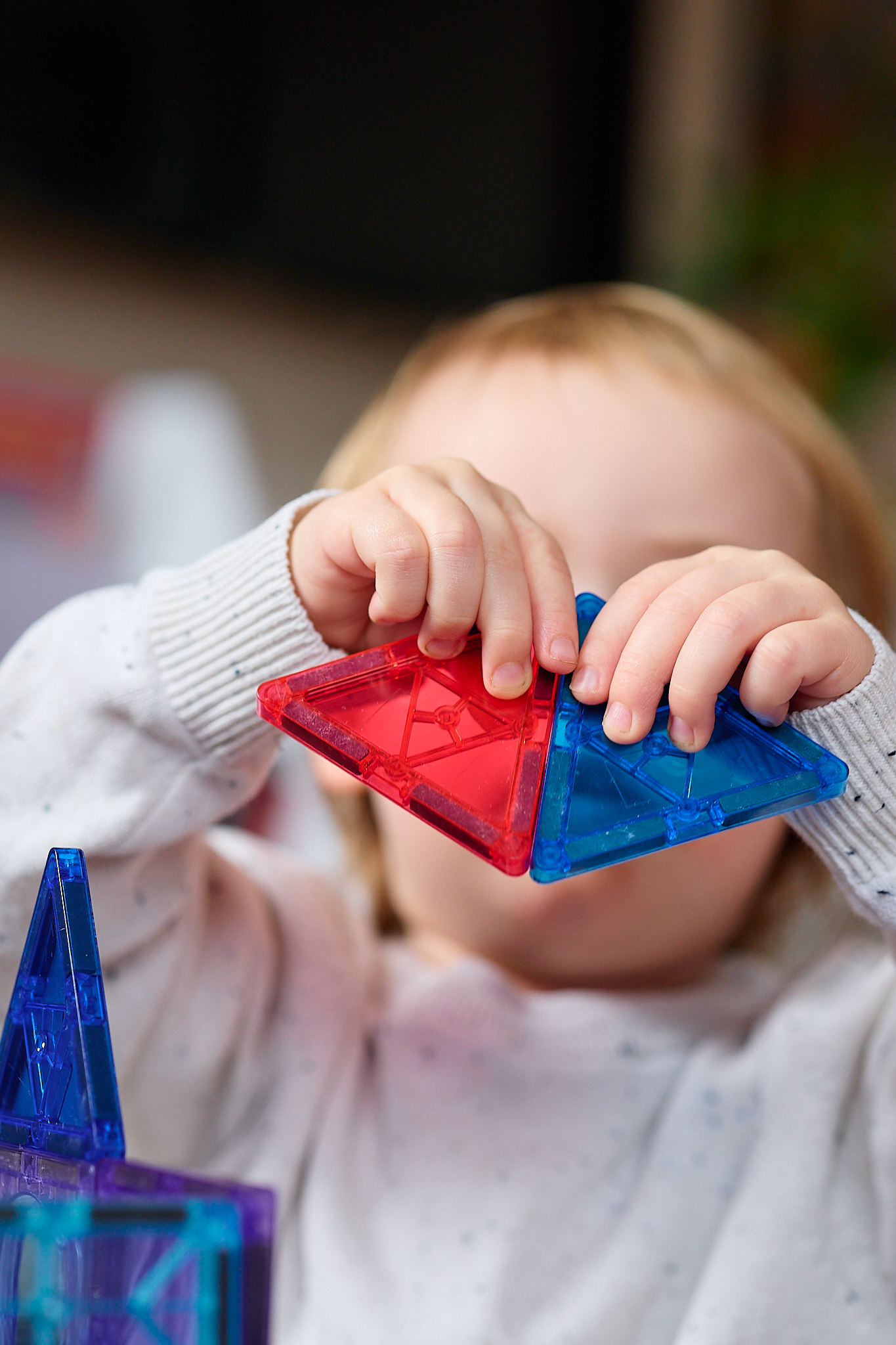 Young child playing with colorful magnetic tile building toys, holding red and blue triangular pieces.