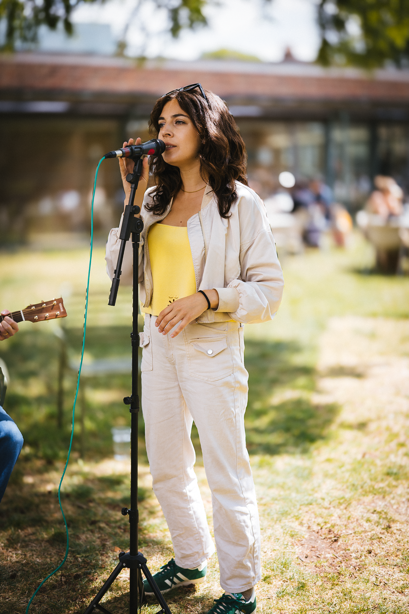 A performer in white attire sings into a microphone during an outdoor event.
