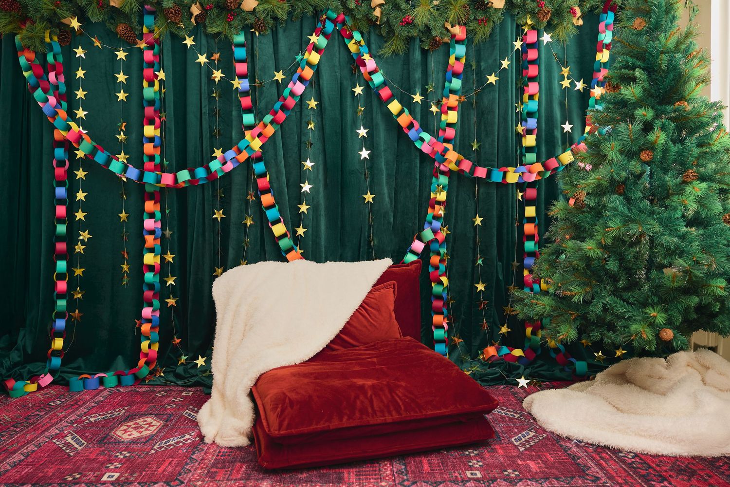 Festive Christmas photo backdrop with colorful paper chain garlands, star decorations, green curtains, and a red velvet cushioned seat.