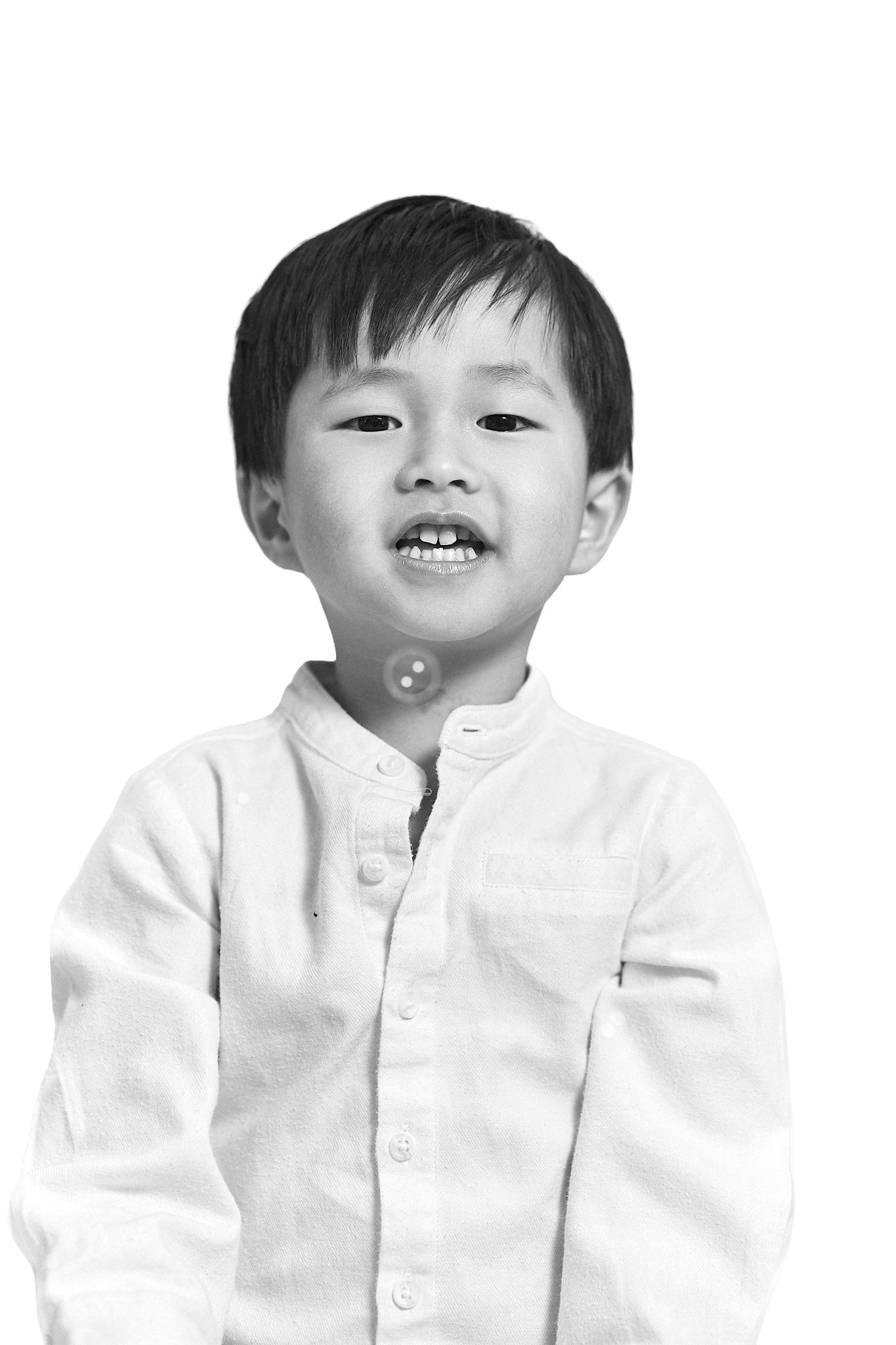 Black and white portrait of a young Asian boy in a white button-up shirt smiling against a white background.