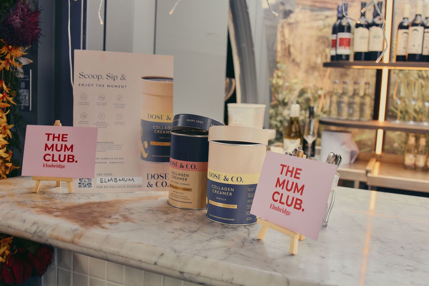 The Mum Club branded display with Dose & Co collagen products on a marble counter at an event.