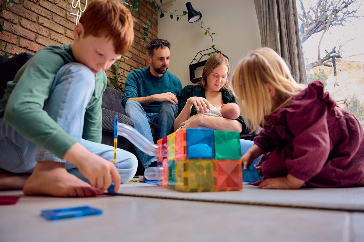 Family with two children playing with colorful magnetic tiles together on living room floor at home.