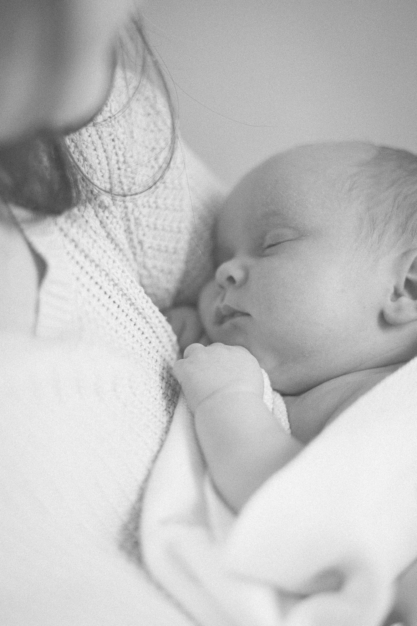 Gentle black and white photograph of parent and infant in soft natural light.