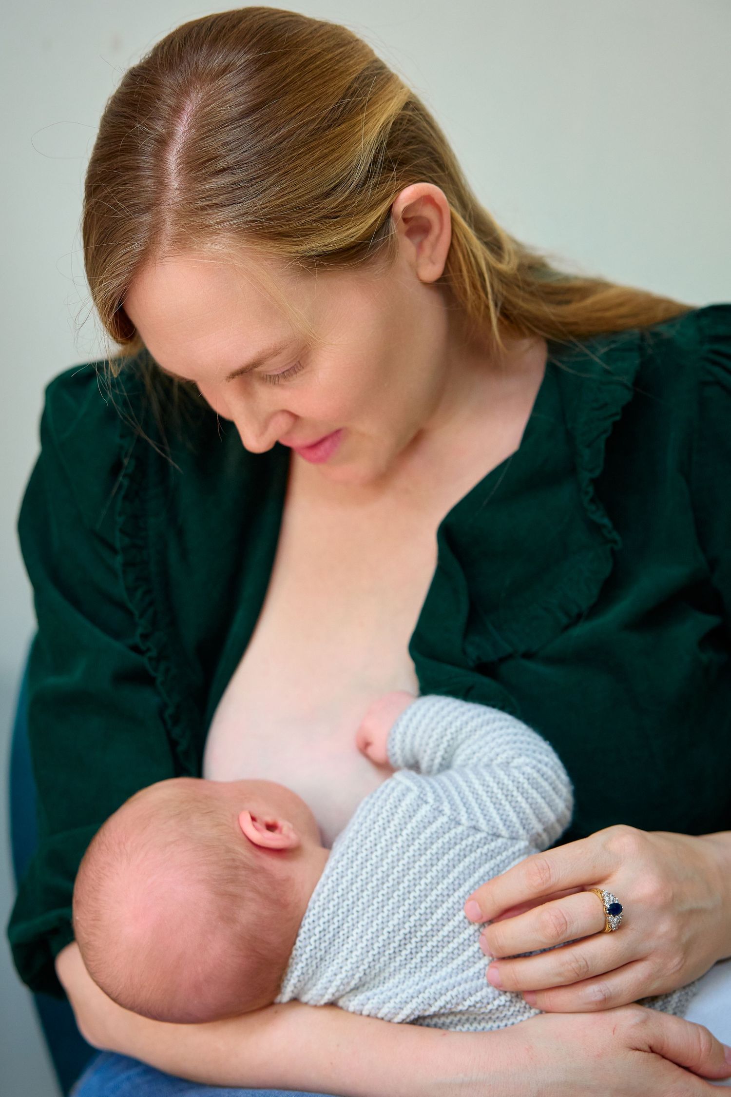 Mother breastfeeding newborn baby while seated, wearing green blouse.