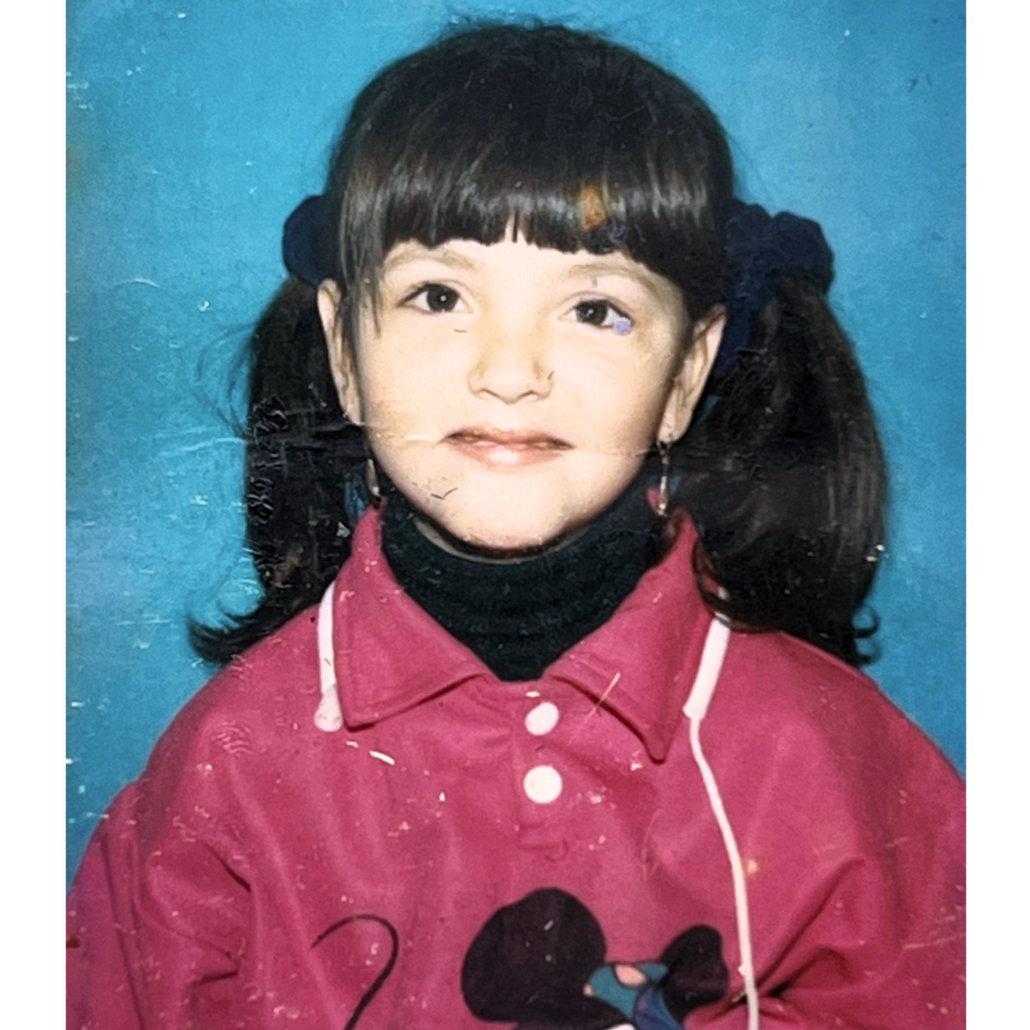A vintage school photo showing a child wearing a red coat with black collar and bangs hairstyle.