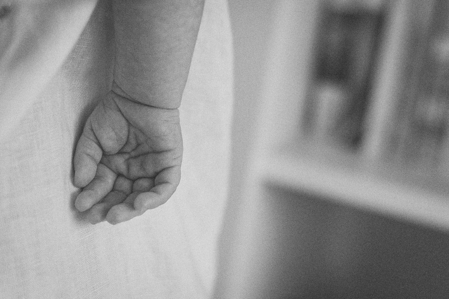 Close-up black and white photo of a baby's tiny hand hanging gently at their side.