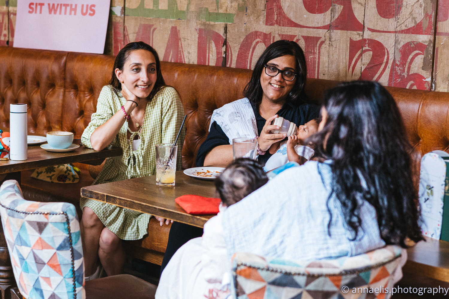 A social gathering of parents and babies in a restaurant with vintage signage.