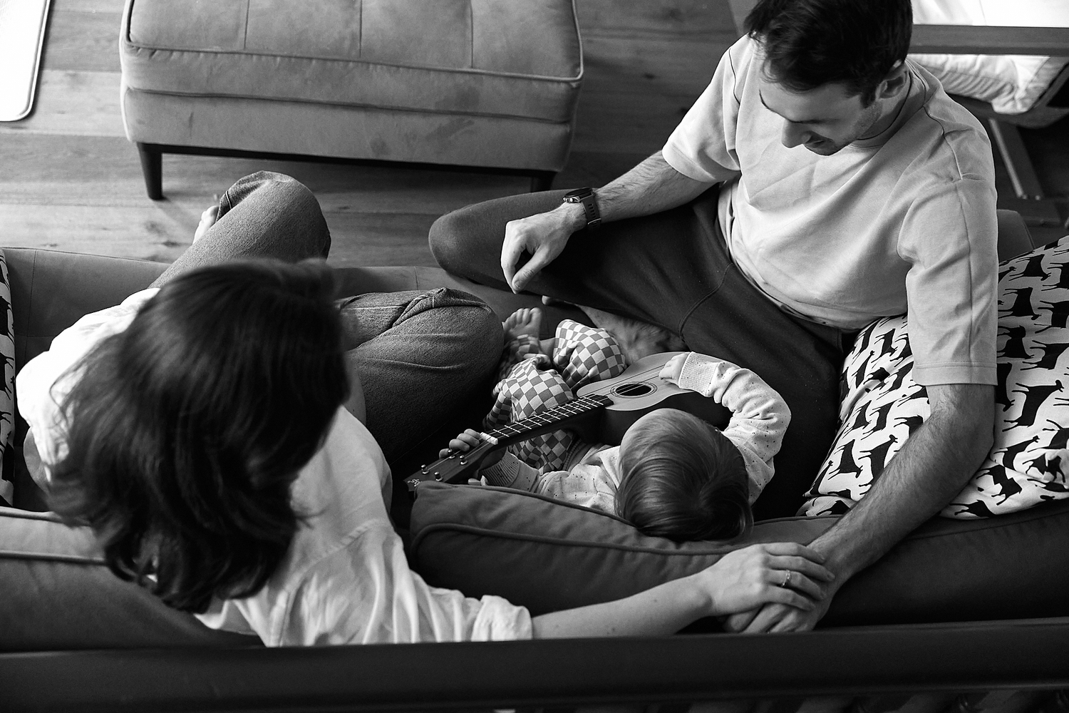 Black and white photo of a family relaxing together on a couch, parents bonding with their baby at home.