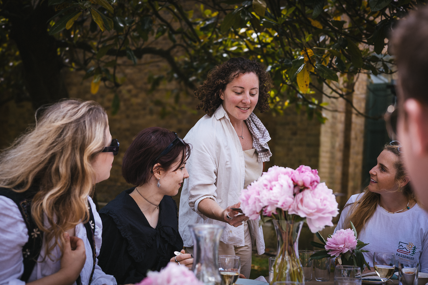 A group enjoys an outdoor gathering with pink flowers and refreshments on a sunny day.