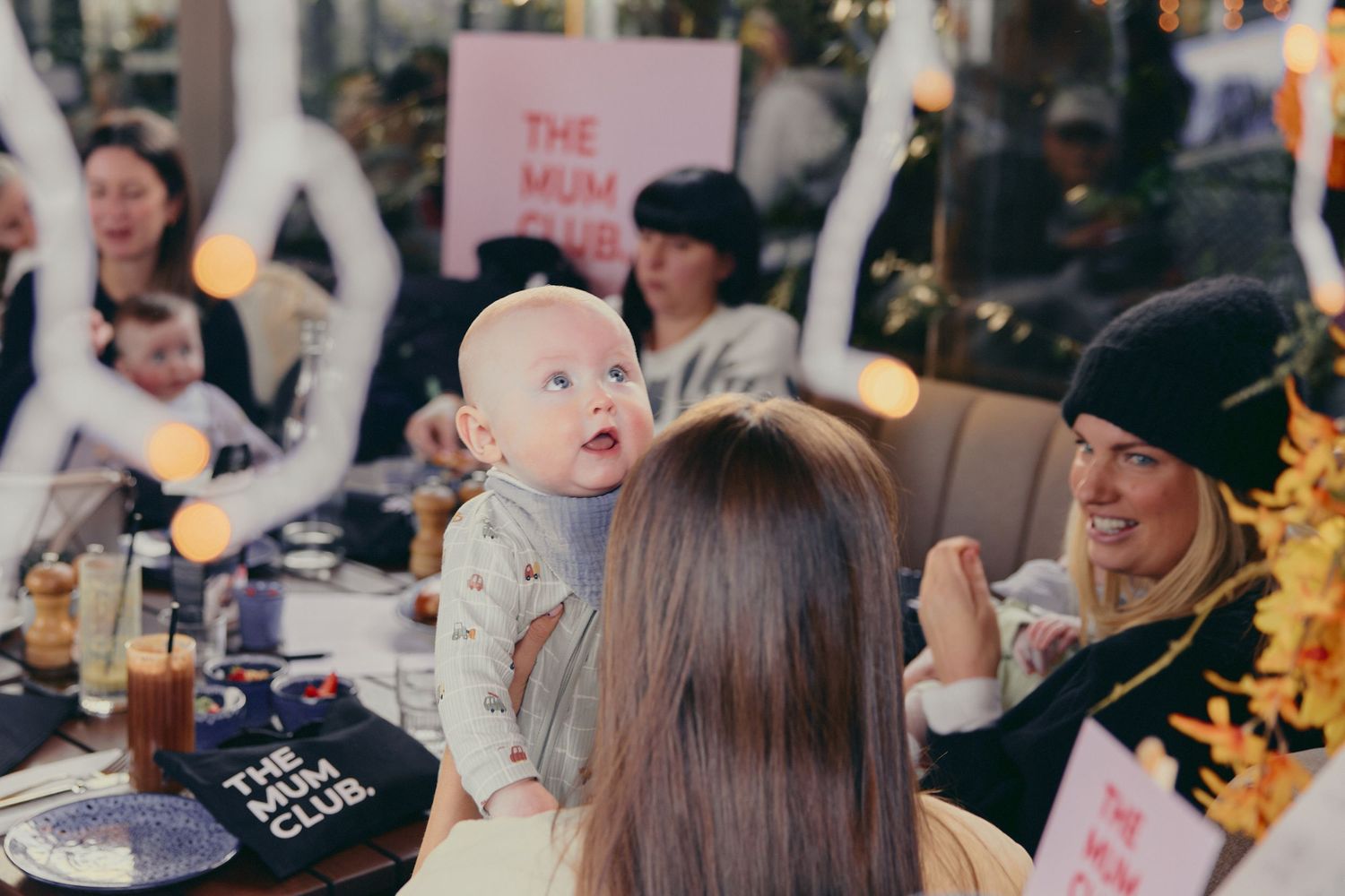 Mother holding baby at The Mum Club social dining event with other mums.