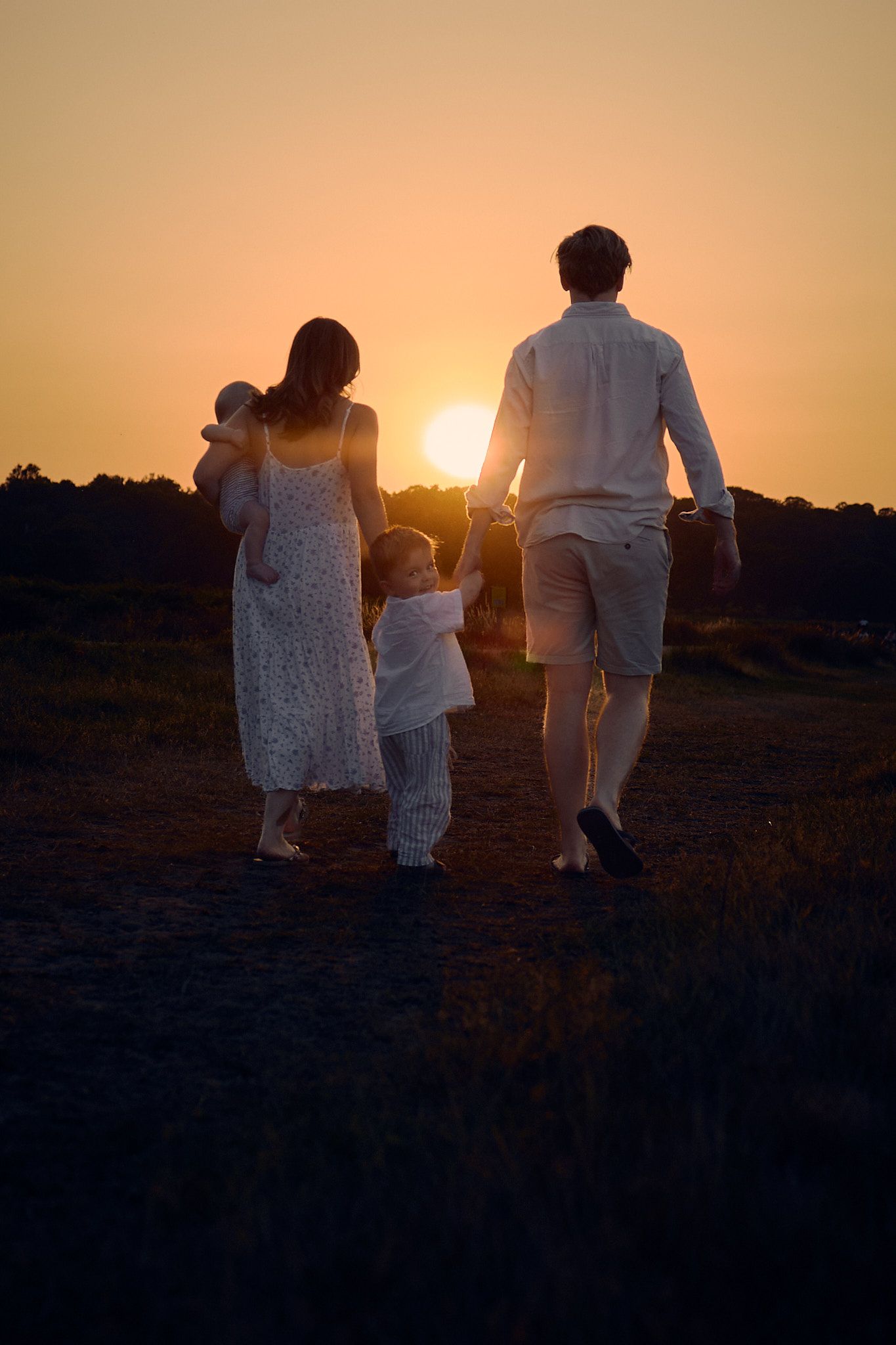 A family walks together towards a golden sunset in a field.