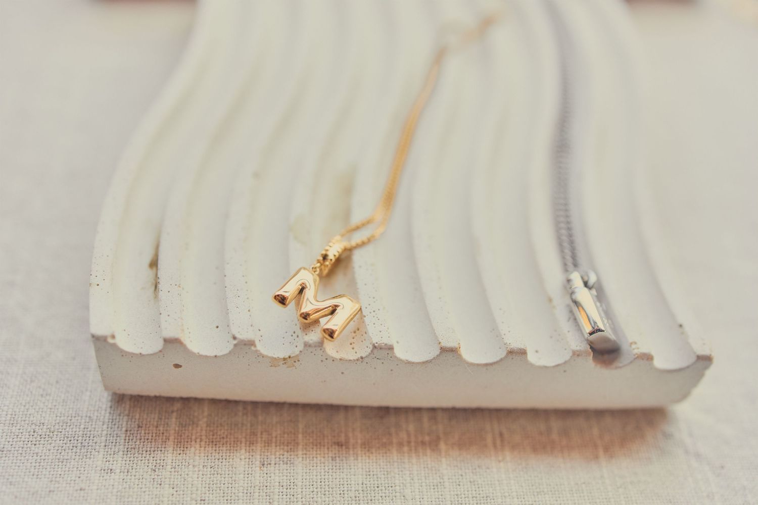 Gold letter M initial necklace displayed on a white jewelry tray with a delicate chain.