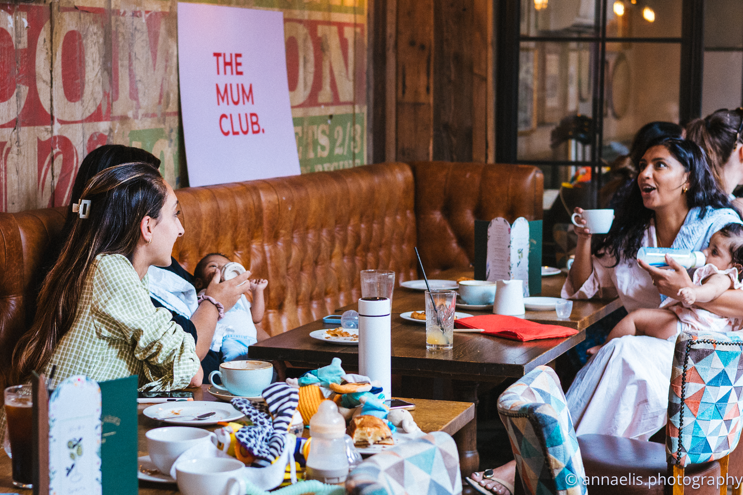 Parents and infants attend a casual meetup in a rustic cafe setting.