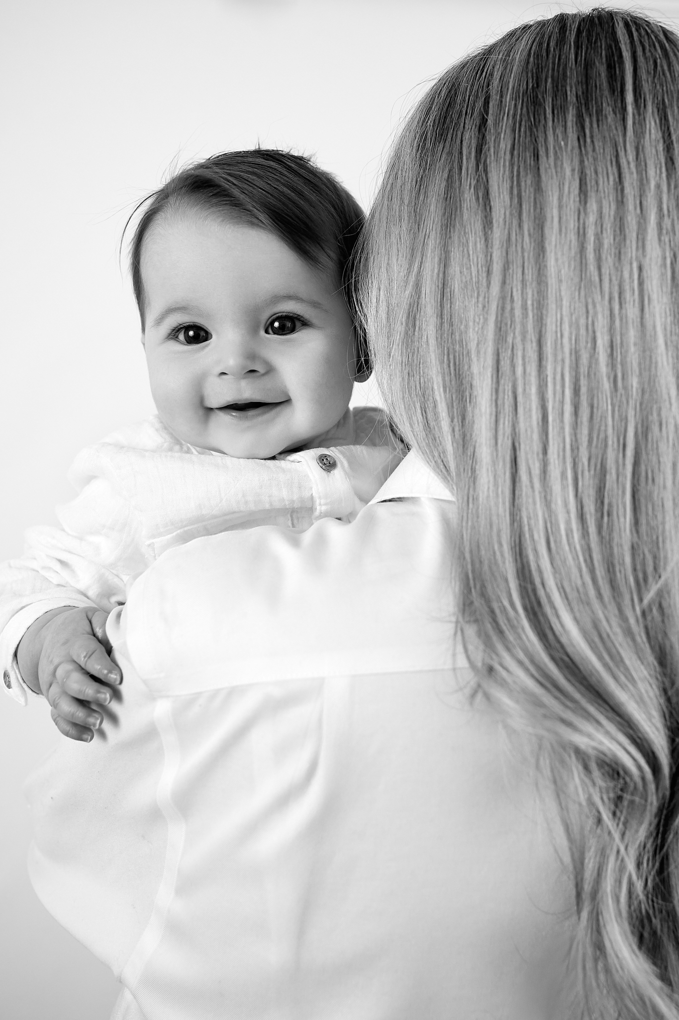 Black and white photo of a smiling baby being held by a blonde woman in a white shirt.