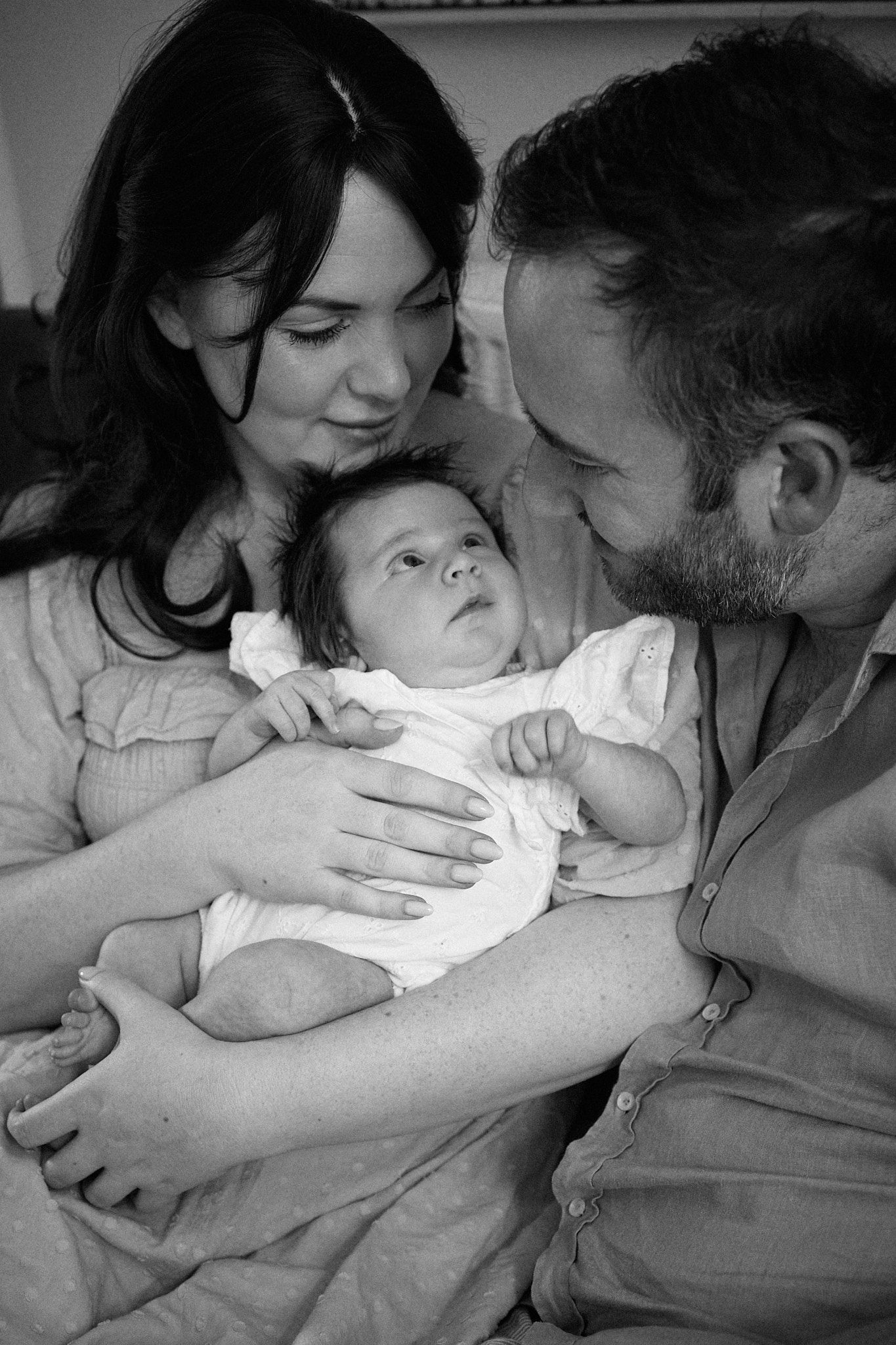 An intimate black and white portrait of a family sharing a tender moment with their newborn baby.