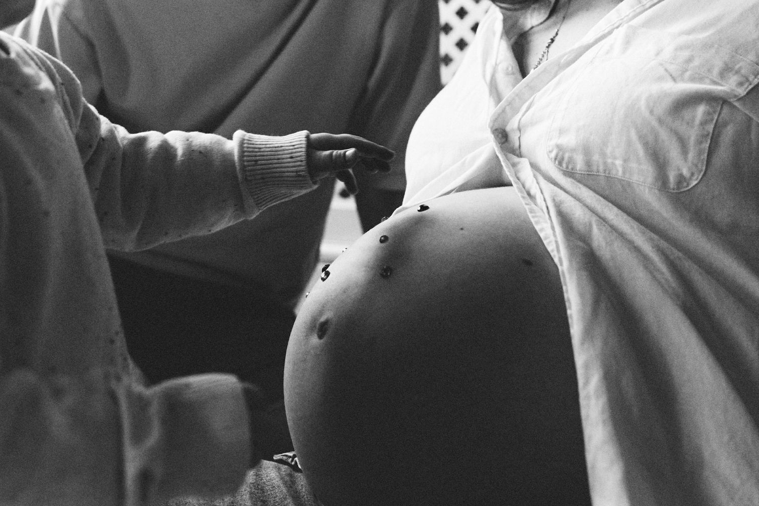 Black and white photo of a pregnant woman's bare belly being touched by a child's hand.