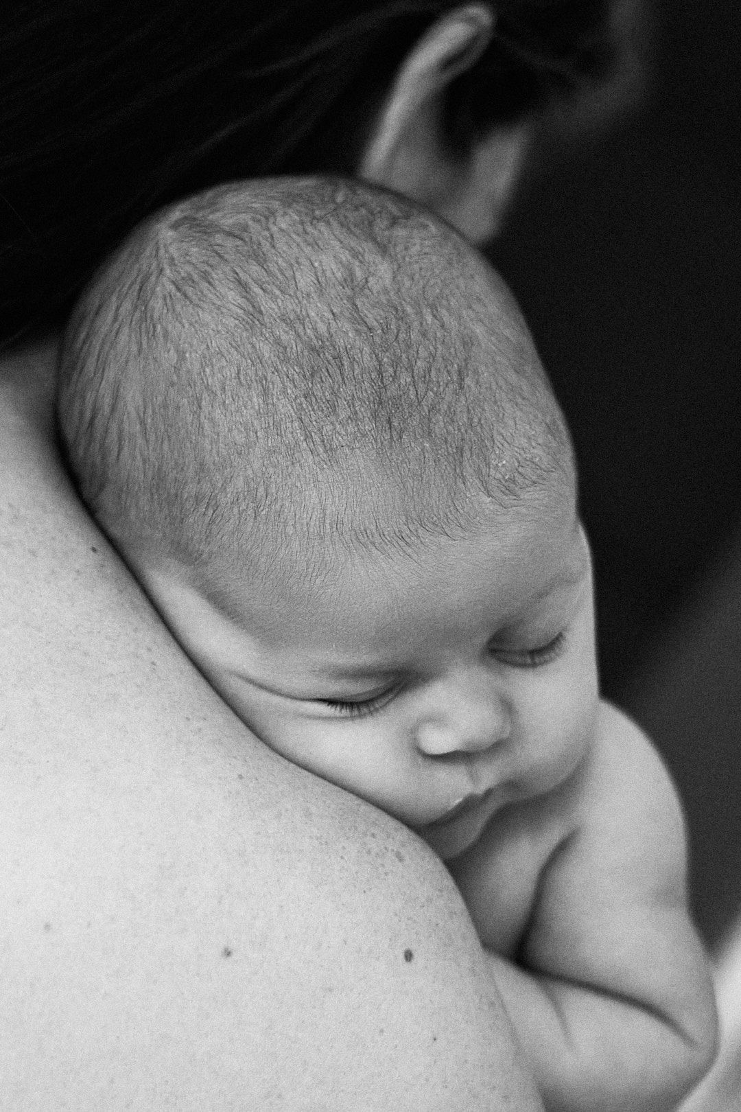 Black and white photo of a sleeping newborn baby resting peacefully on a mothers shoulder.