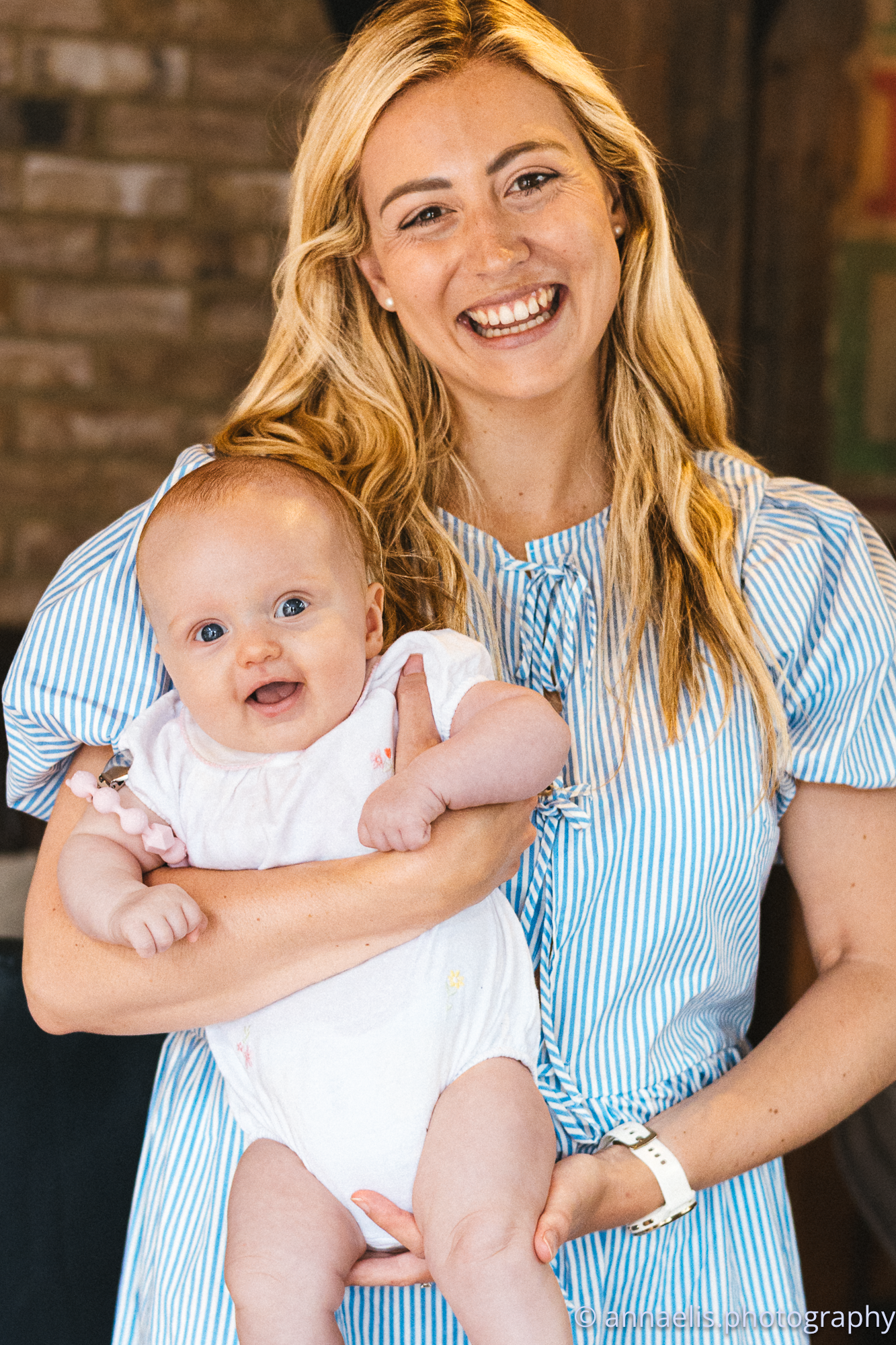 Parent in striped dress sharing happy moments with infant in white outfit.