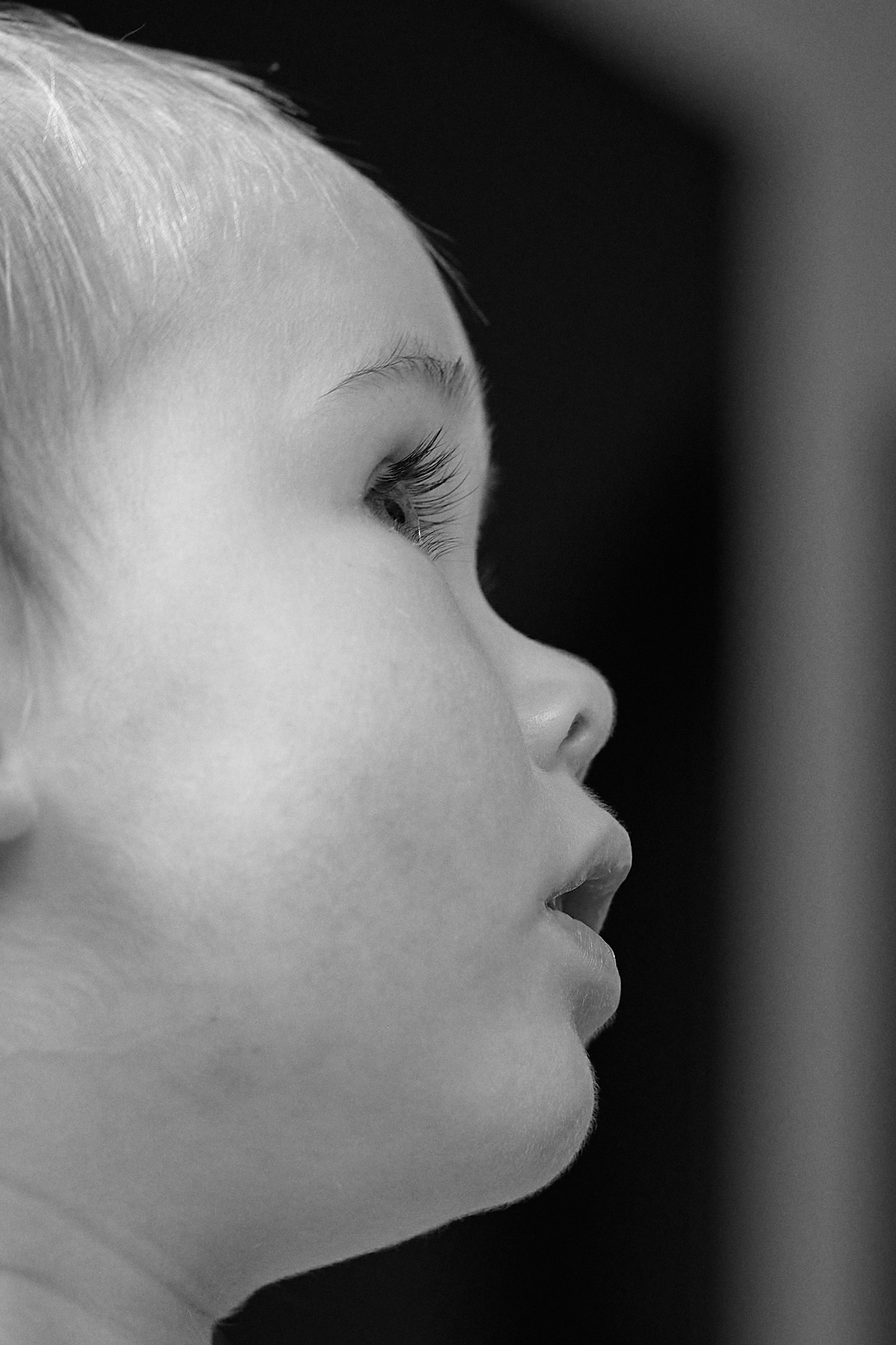 Black and white close-up profile portrait of a young blonde child looking upward with long eyelashes.