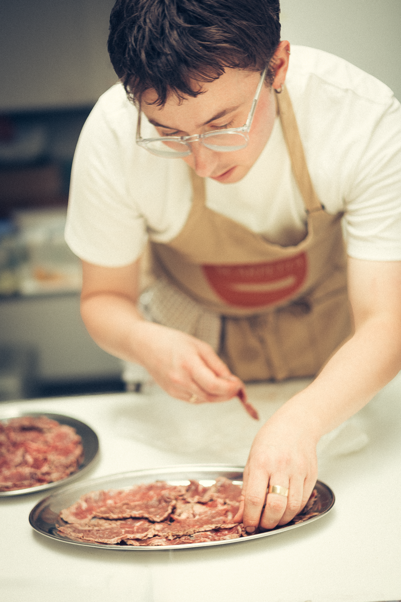 Chef in apron carefully arranging meat on silver platter in professional kitchen.
