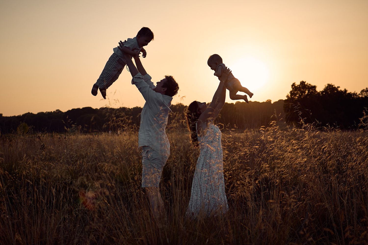 Silhouette of a family lifting two children against a golden sunset in a field.