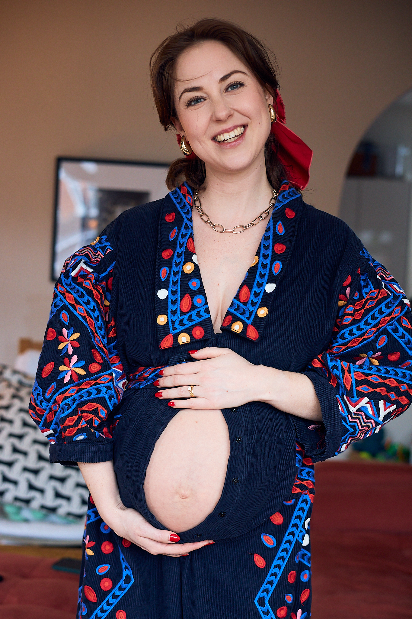 A person in a navy dress with colorful embroidered details poses in a maternity photoshoot series.